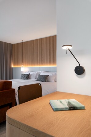 Ein Hotelzimmer mit einem Bett, einem Nachttisch mit einem Buch, einem Sessel und einer Wandlampe.