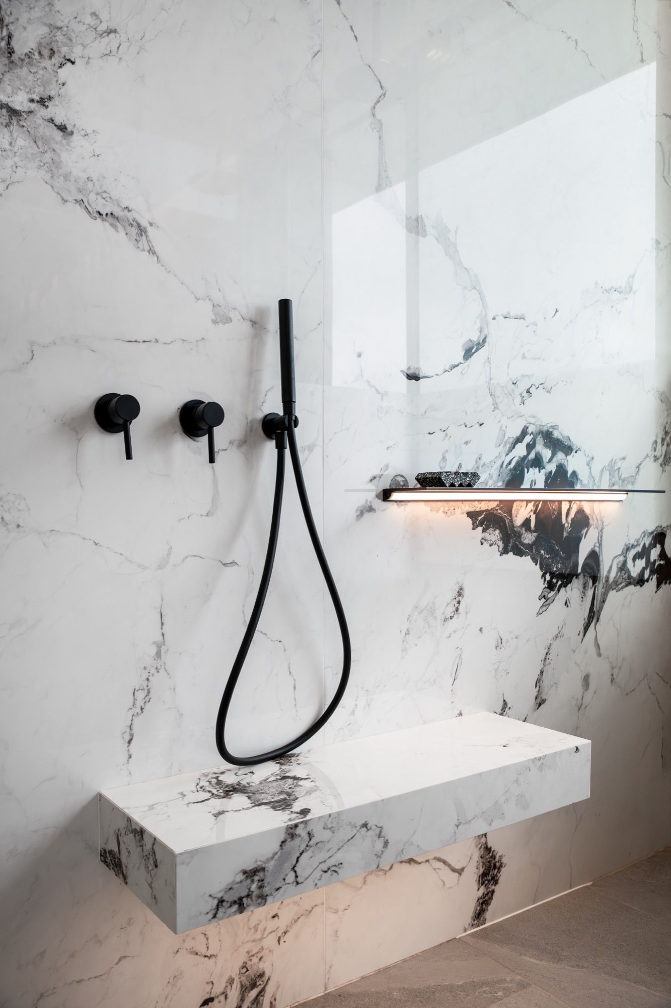 A modern bathroom with a marble wall, a built-in sink, and a handheld showerhead.
