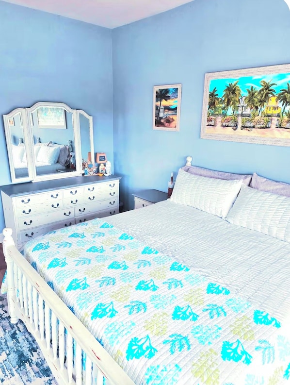 A bedroom with a bed, a dresser, a mirror, and a painting on the wall. - Sunset Palms Pool & Hot Tub with Game Room (Cape Coral)
