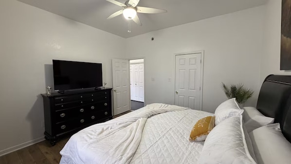 Ein Schlafzimmer mit Bett, Kommode, Fernseher und Deckenventilator.