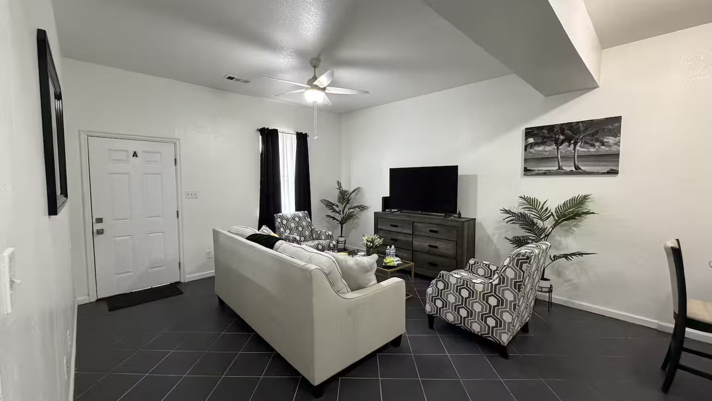 A living room with a sofa, armchairs, a TV, and a ceiling fan.