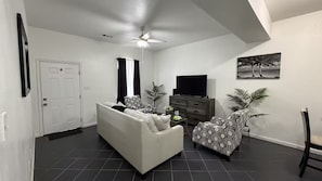 Ein Wohnzimmer mit Sofa, Sesseln, Fernseher und Deckenventilator.