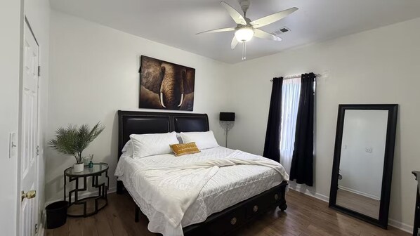 A bedroom with a bed, a ceiling fan, a window with curtains, a door, and a wall-mounted picture.