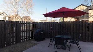 An outdoor patio with a red umbrella, a covered grill, and a table with chairs.