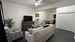 Ein Wohnzimmer mit einer Couch, einem Fernseher, einem Couchtisch und einem Deckenventilator.