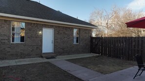 A brick house with a white door, a wooden fence, and a red umbrella. - The Spot on Warner Ste A close to downtown JBO (Jonesboro)