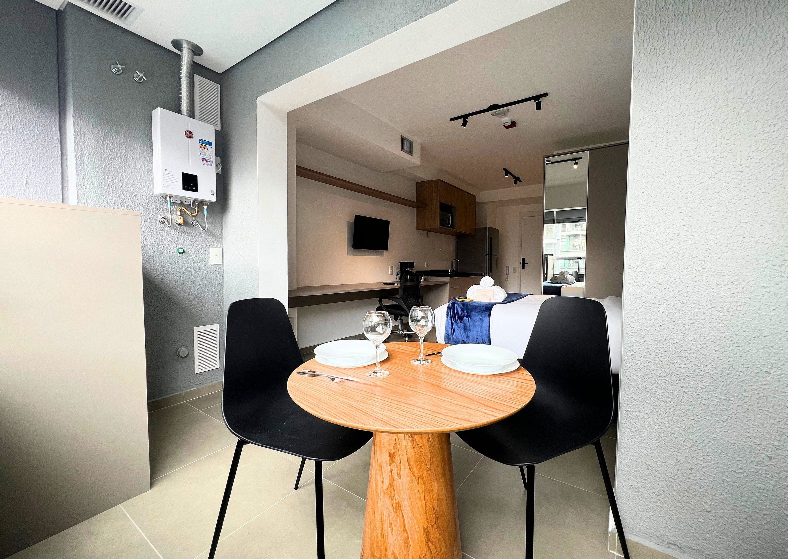 A modern hotel room with a dining area, a bed, a TV, and a kitchenette.