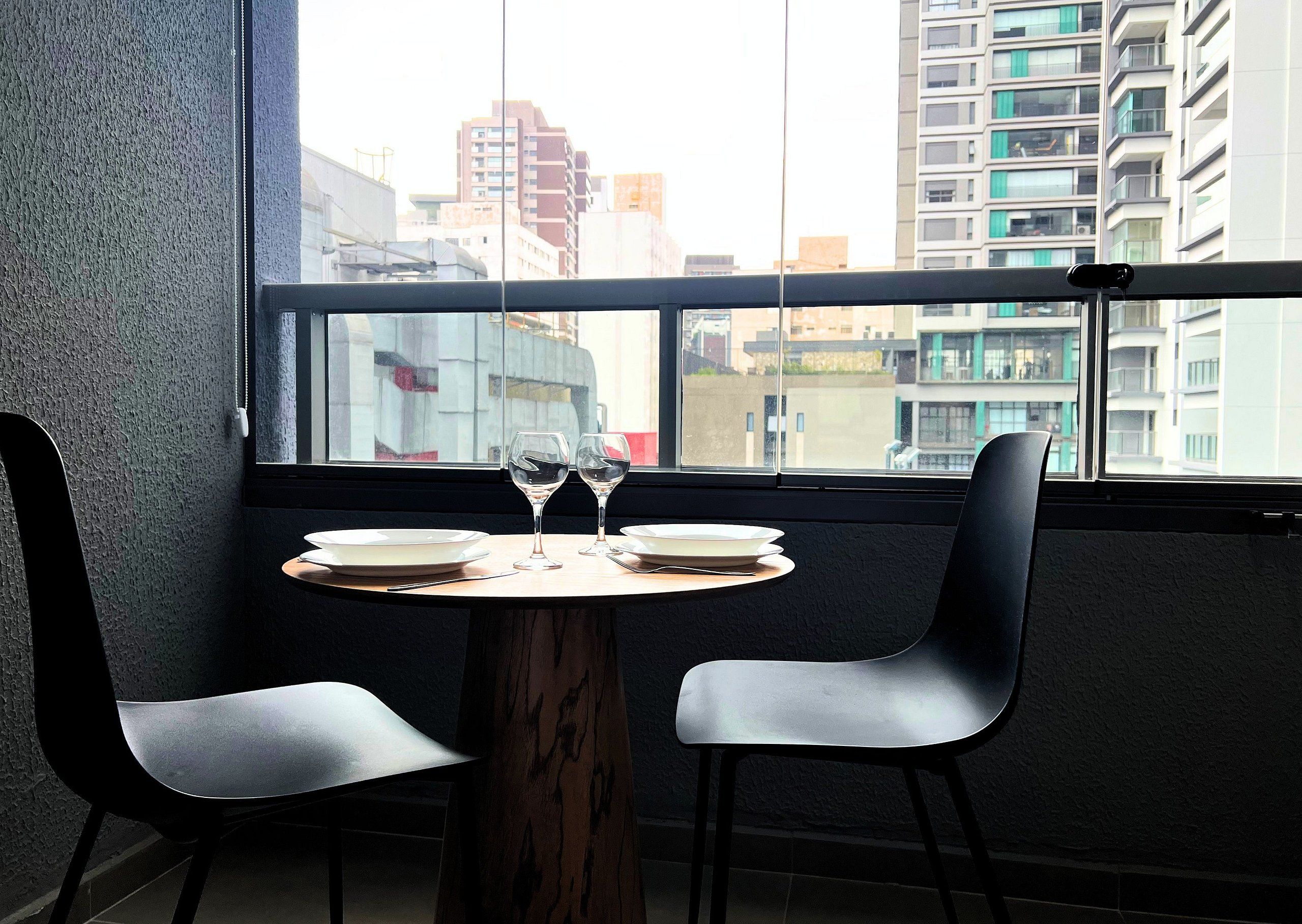 Una mesa de comedor con dos sillas, un ventanal con vistas a edificios y un teléfono en la pared.