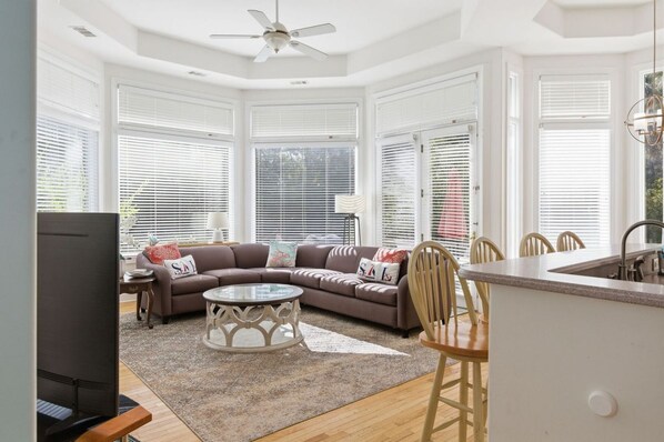 A modern living room with a sofa, coffee table, and dining area with chairs. - Coastal Escape w/ Putting Green, Pool, + Hot Tub (Hilton Head Island)