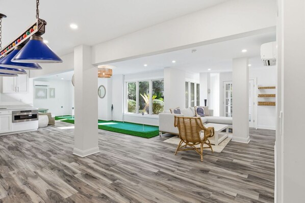A modern interior with a pool table, a sofa, and a dining area. - Coastal Escape w/ Putting Green, Pool, + Hot Tub (Hilton Head Island)