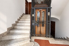 A staircase leading to a door with a metal gate, a wooden door, and a red mat at the bottom. - Elegantis Casa Flavia in Trastevere With Terrace  (Roma)