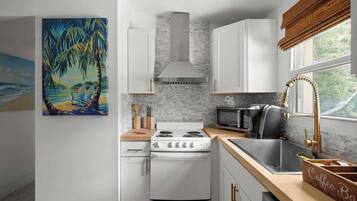 Une cuisine moderne avec des meubles blancs, une cuisinière, un four à micro-ondes et un évier doté d’un robinet doré.