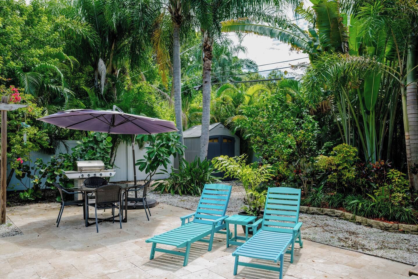 An outdoor patio with a grill, chairs, and an umbrella.