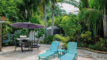 An outdoor patio with a grill, chairs, and an umbrella.