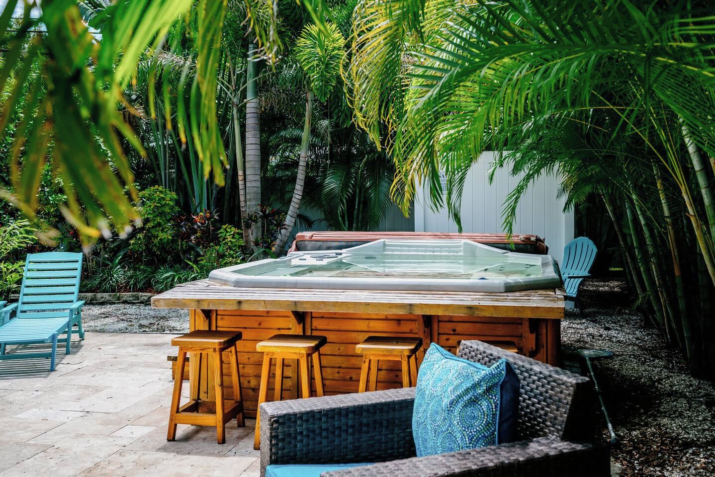Un bain à remous entouré de meubles et de chaises en bois, dans un cadre de jardin tropical.