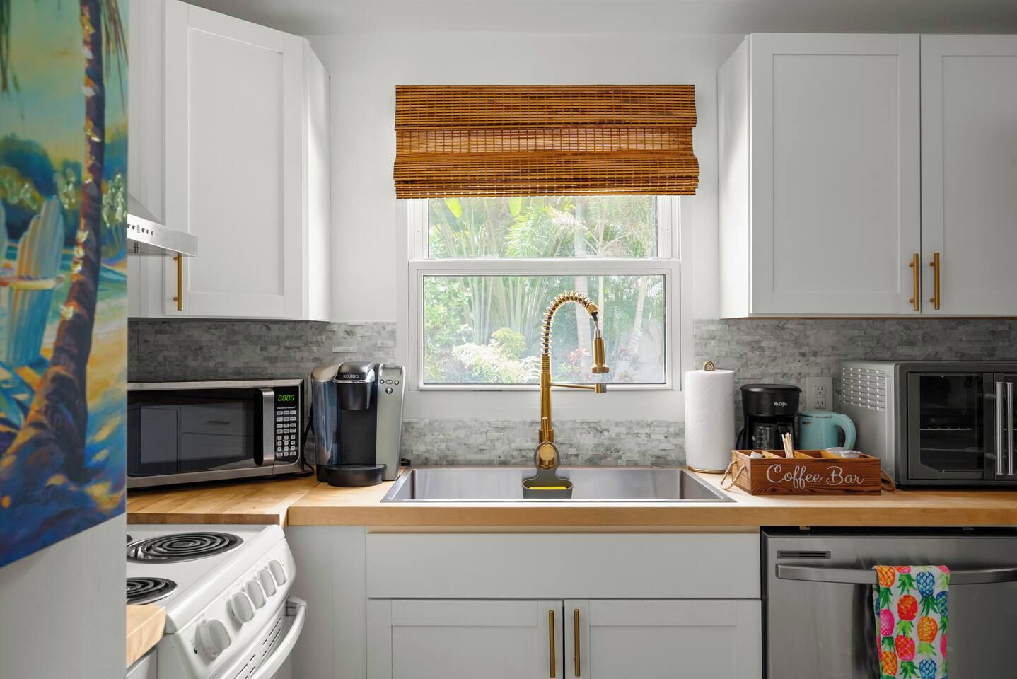 A kitchen with white cabinets, a stainless steel sink, a coffee maker, a microwave, and a stove.