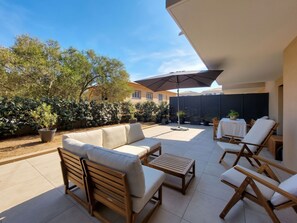 Un patio con un sofá, sillas y una mesa. Hay un área cubierta con una sombrilla.