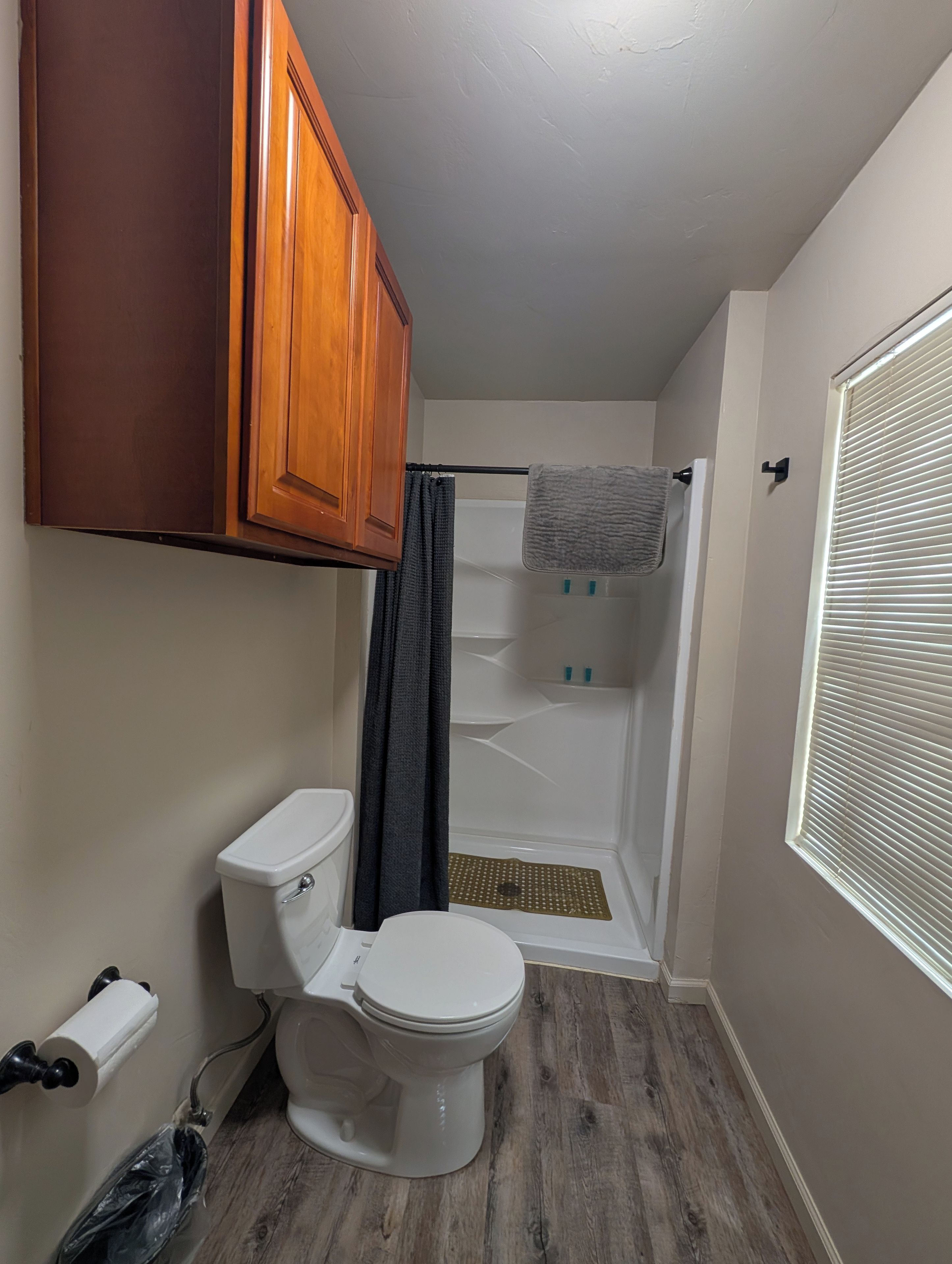 Een badkamer met toilet, douche en een raam met zonwering.