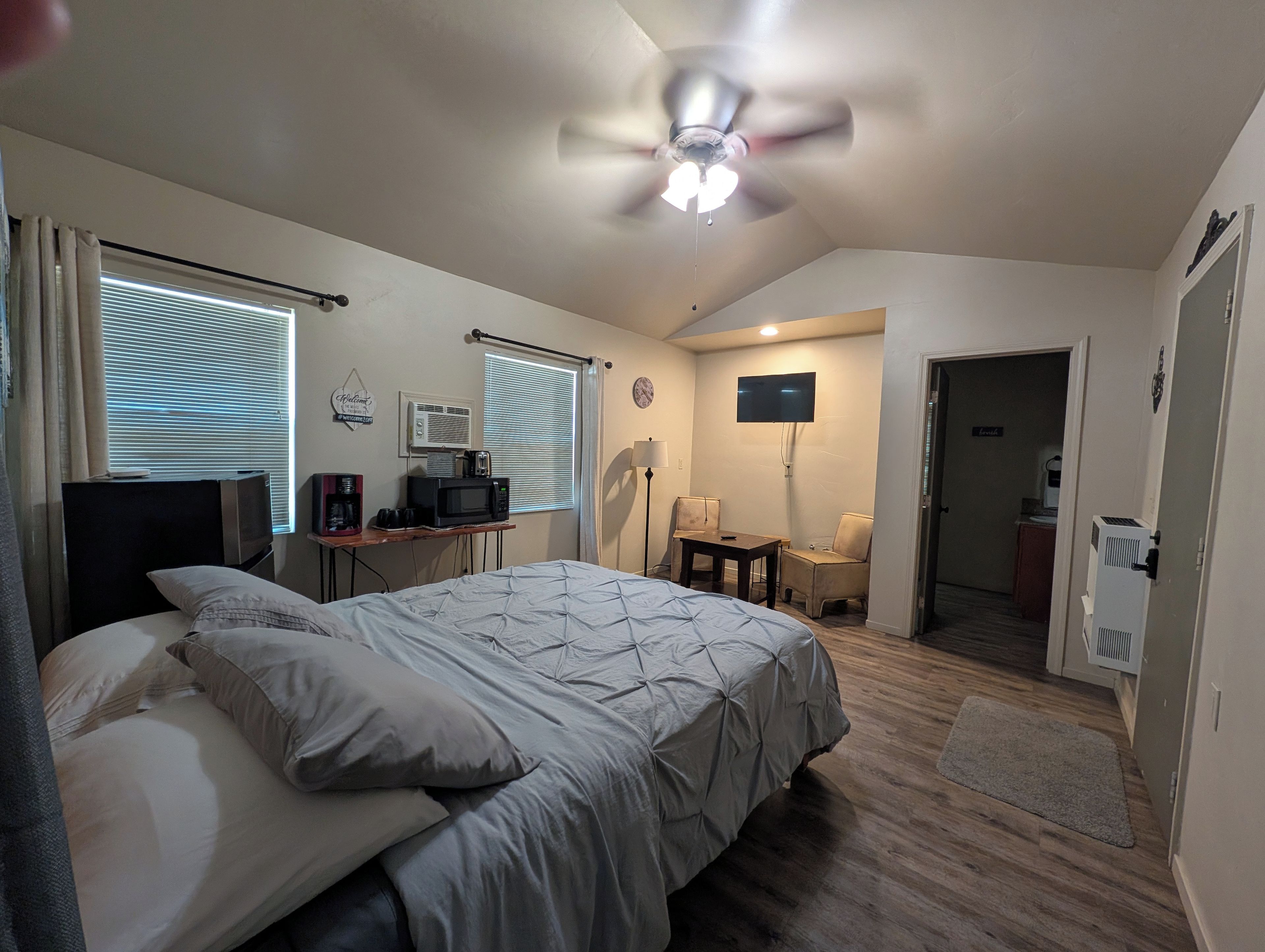 A bedroom with a bed, a desk, a TV, and a ceiling fan.