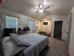 A bedroom with a bed, a desk, a TV, and a ceiling fan.