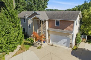 A two-story house with a garage, a stone facade, and a well-maintained lawn. - Lake House for 14 · Hot Tub, Fire Pit & Garden Dome · 18–20 min to Indiana Dunes National Park (Valparaiso)