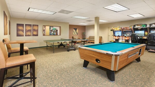 Une table de billard recouverte d’un drap vert, une table de ping-pong et un espace détente avec des chaises et une table.