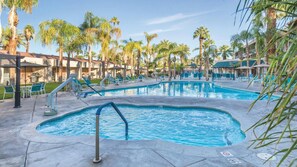 Un espace piscine comprenant plusieurs piscines, des chaises longues et des palmiers.