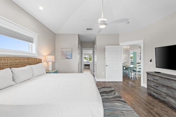 A bedroom with a large bed, a nightstand, a lamp, a ceiling fan, and a TV. - Bleu Rivage – Private Pool Retreat (Cape San Blas)