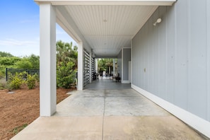 A covered outdoor area with a concrete floor, a white ceiling, and a view of a garden with palm trees. - Bleu Rivage – Private Pool Retreat (Cape San Blas)