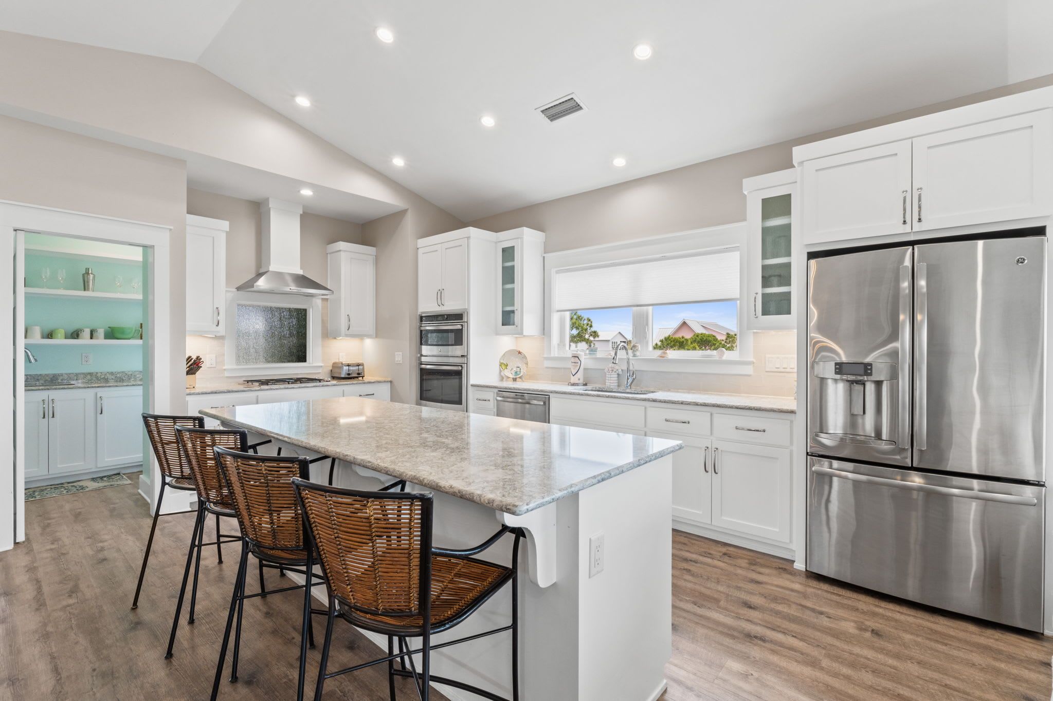A modern kitchen with white cabinetry, stainless steel appliances, and a central island with bar stools.