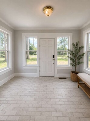 A room with a white door, two windows, a bench, and a potted plant. - Annie A’s- Downtown Port St. Joe Cottage: Pet Friendly + Boat Parking (Port St. Joe)
