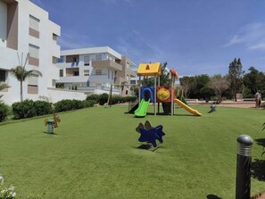 Ein Spielplatz mit Rutschen und Klettergerüsten, umgeben von gepflegtem Rasen und einem Gebäude im Hintergrund.