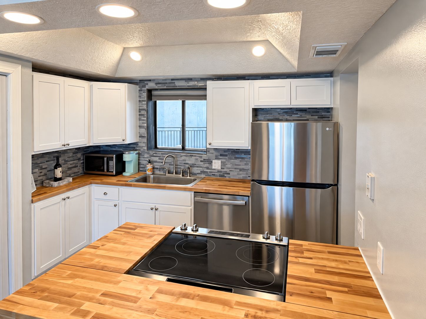 A modern kitchen with white cabinets, a stainless steel refrigerator, a built-in microwave, and a wooden countertop.