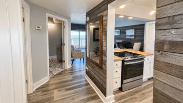 A modern kitchen with a built-in oven, a dining area with a table and chairs, and a view of the ocean through a large window.
