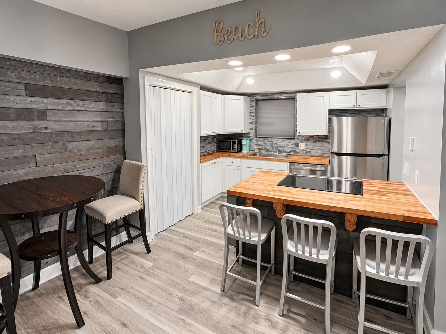 Une cuisine moderne avec des meubles blancs, un îlot central en bois et un four à micro-ondes encastré.