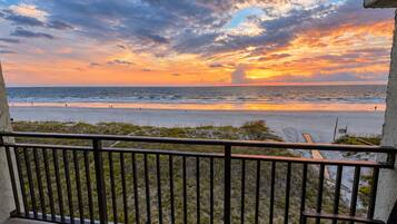 Un balcon avec vue sur la plage et l’océan au coucher du soleil.