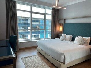 A hotel room with a large bed, a desk, and a view of a cityscape through large windows. - Vesta - Superior Suite - 2BR - Nile View (Cairo)