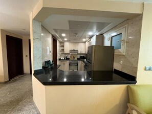 A modern kitchen with a central island, built-in appliances, and a marble backsplash. - Vesta - Executive Suite - 2BR - Partial Nile View (Cairo)