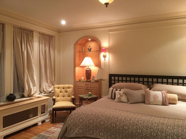 Een hotelkamer met een bed, een stoel, een nachtkastje met lampen en decoratieve wandbekleding.