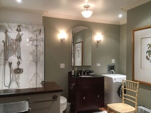 Een badkamer met een marmeren douche, een donker houten wastafelmeubel, een toilet, een wasmachine en een stoel.