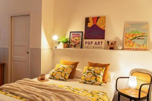 A hotel room with a bed, a chair, a lamp, and wall art including a poster of Andy Warhol's Pop Art and a poster of a cityscape. - Palazzo Bevilacqua Rooms (Naples)