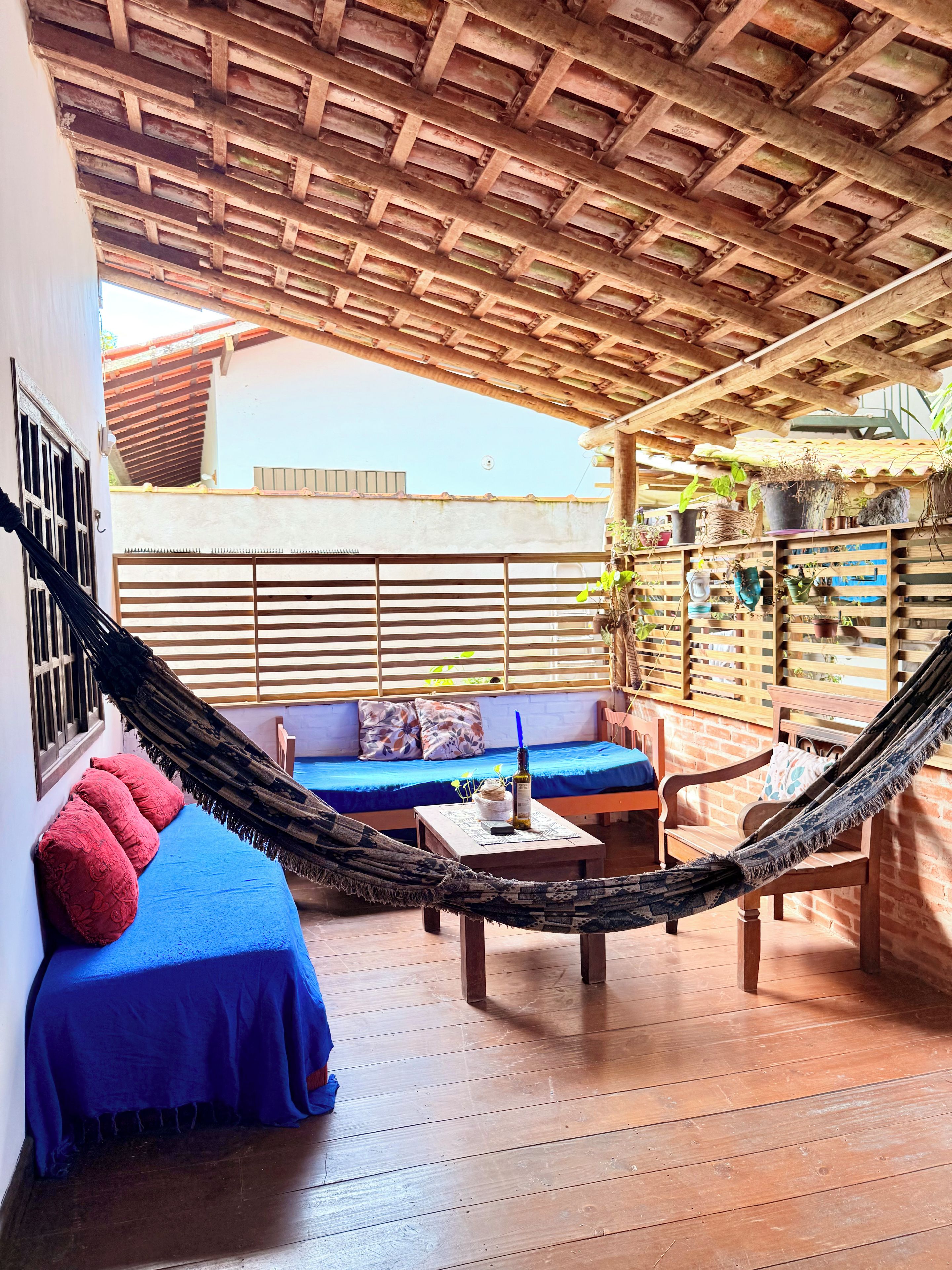A hammock, a blue sofa, and a wooden table in a covered outdoor seating area.