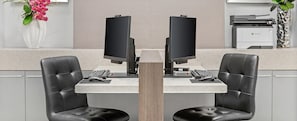 Un poste de travail équipé de deux écrans, d’une imprimante, de deux fauteuils en cuir et d’un vase avec des fleurs.