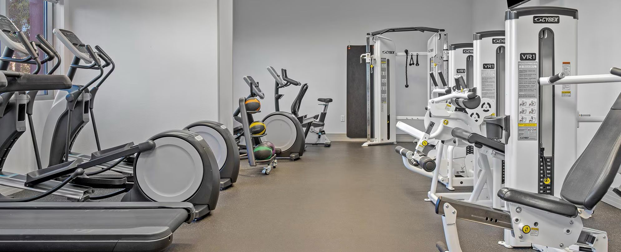 Une salle de sport équipée de divers appareils d’exercice, notamment des tapis de course, des appareils elliptiques et des appareils de musculation.