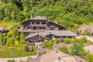 A large, multi-story wooden house with a balcony, surrounded by lush greenery. - Chalet X – 15 people – Montriond (Montriond)