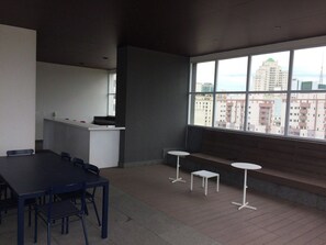 A modern interior with a dining table, chairs, a small kitchen area, and a large window offering a city view. - Studio London near Paulista w/ Parking LA804 (São Paulo)
