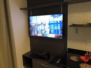 Un téléviseur fixé au mur, avec un espace cuisine en dessous, comprenant un plan de travail et un meuble.