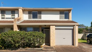 A two-story residential building with a garage, a covered porch, and a well-maintained front yard. - Illa Villa is a charming townhouse just 50 meteres from Reddall Reserve. (Lake Illawarra)