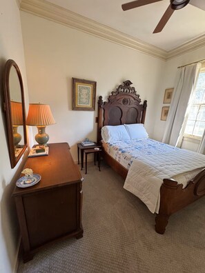 A bedroom with a wooden bed, a bedside table, a lamp, a mirror, and a framed picture on the wall. - Historic Cottage near MSU, Old Waverly & Mossy Oak (West Point)