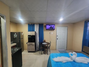 A hotel room with a bed, a TV, a kitchenette, and a dining area. - Affordable, self contained studio, 8-10 mins from the Piarco Intl Airport (Arima)